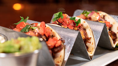 three tacos with pico de gallo on top with guacamole on the side
