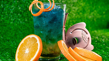 blue and green cocktail surrounded by orange slices and bartender tools