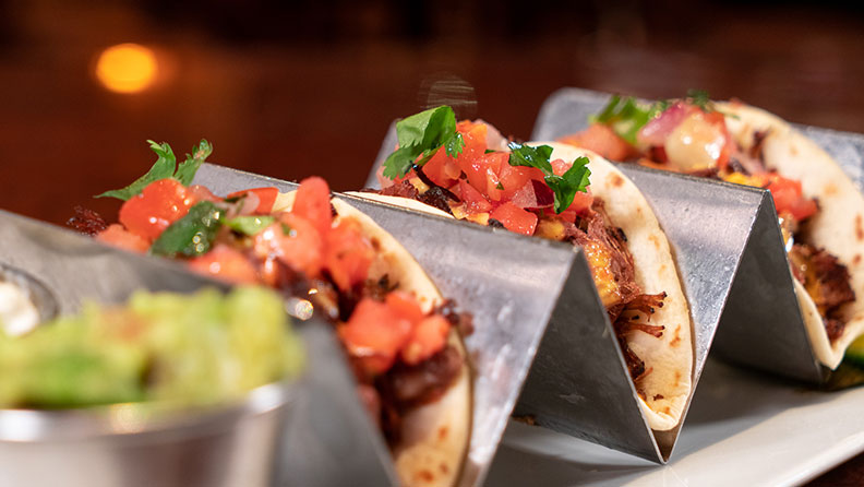 three tacos with pico de gallo on top with guacamole on the side