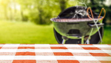 outdoor dining with red and white checkered tablecloth and blurred smoking grill